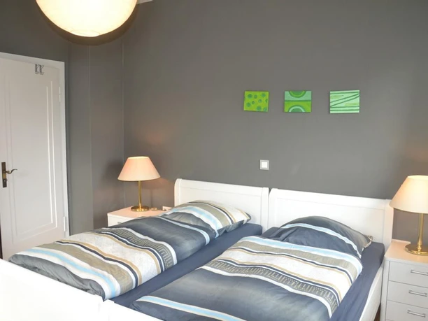 Zwei Einzelbetten mit moderner Bettwäsche in einem schlichten, grauen Schlafzimmer mit Wanddekoration.