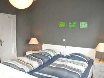 Ferienwohnungen Tal-Residenz Bad Salzuflen: Schlafzimmer 2 Zwei Einzelbetten mit moderner Bettwäsche in einem schlichten, grauen Schlafzimmer mit Wanddekoration.