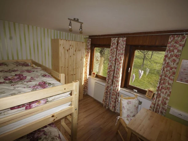 Helles Kinderzimmer mit Etagenbett, Naturholzmöbeln und Ausblick auf eine grüne Landschaft.