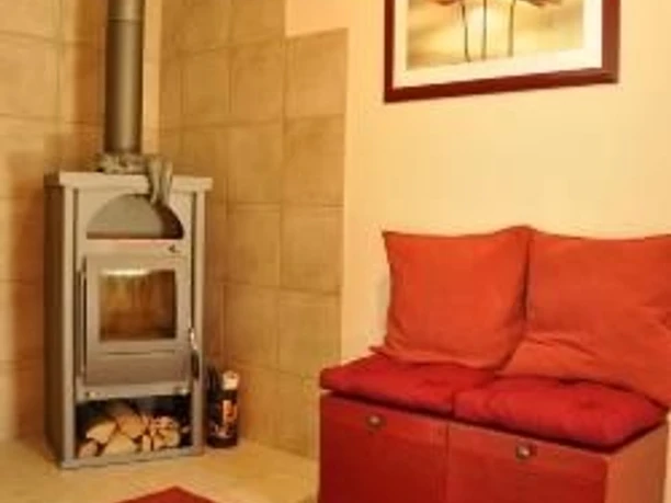 Warmer Eingangsbereich mit rotem Teppich, einem Kaminofen und Sitzbank mit roten Kissen.