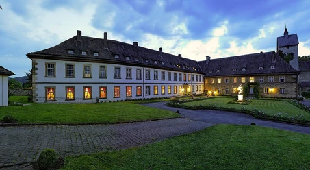 Schloß Gehrden Außenansicht Beleuchtetes Schloss Gehrden bei Dämmerung, umgeben von gepflegtem Rasen und wolkigem Himmel.