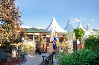 Biergarten Biergarten mit Sonnenschirmen und Sitzplätzen, geschmückt mit Pflanzen, Skulptur in bunter Kleidung.