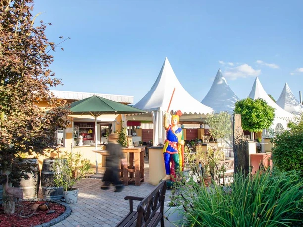 Biergarten Biergarten mit Sonnenschirmen und Sitzplätzen, geschmückt mit Pflanzen, Skulptur in bunter Kleidung.