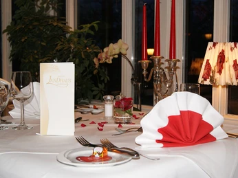 Restaurant Landhaus Schieder Elegantes Gedeck in einem stilvollen Restaurant mit weiß-roter Serviette und romantischer Kerzenbeleuchtung.