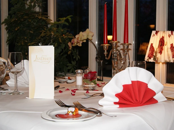 Restaurant Landhaus Schieder Elegantes Gedeck in einem stilvollen Restaurant mit weiß-roter Serviette und romantischer Kerzenbeleuchtung.