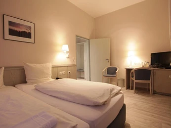 Helles, modern eingerichtetes Doppelzimmer mit zwei Einzelbetten, Schreibtisch, TV und Wandlampe.