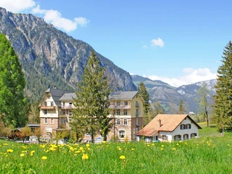 Aussenansicht des Hotels Kurhaus Grimmialp im Sommer Hotelgebäude aus der Belle Epoque inmitten einer blühenden Löwenzahnwiese
