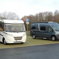 Wohnmobilstellplätze in Herzebrock-Clarholz Zwei Wohnmobile parken auf einem gepflasterten Parkplatz vor kahlen Bäumen unter bewölktem Himmel.