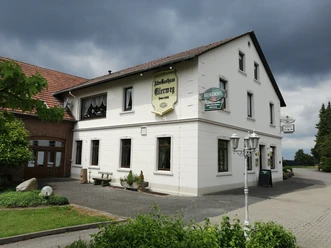 altes_gasthaus_ellerweg_teutoburger-wald-tourismus_bohlken Historisches zweistöckiges Gasthaus mit weißer Fassade, umgeben von gepflastertem Hof und grüner Landschaft.