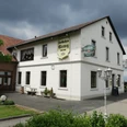 altes_gasthaus_ellerweg_teutoburger-wald-tourismus_bohlken Historisches zweistöckiges Gasthaus mit weißer Fassade, umgeben von gepflastertem Hof und grüner Landschaft.