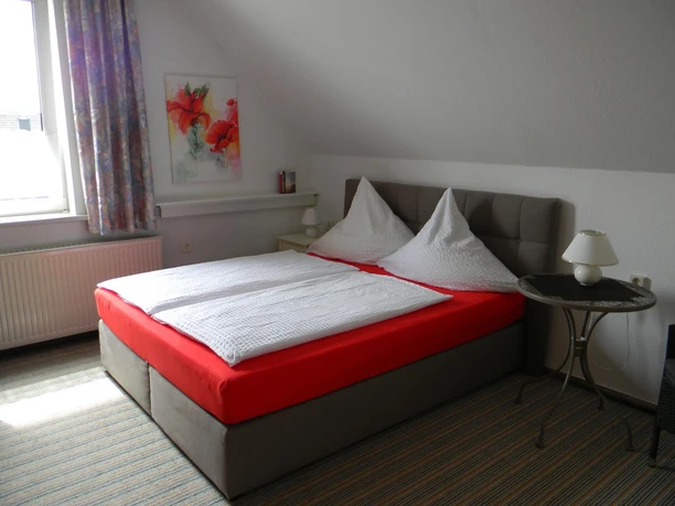 Helles Gästezimmer mit Doppelbett, farbenfrohem Bild an der Wand und Tageslicht durch großes Fenster.