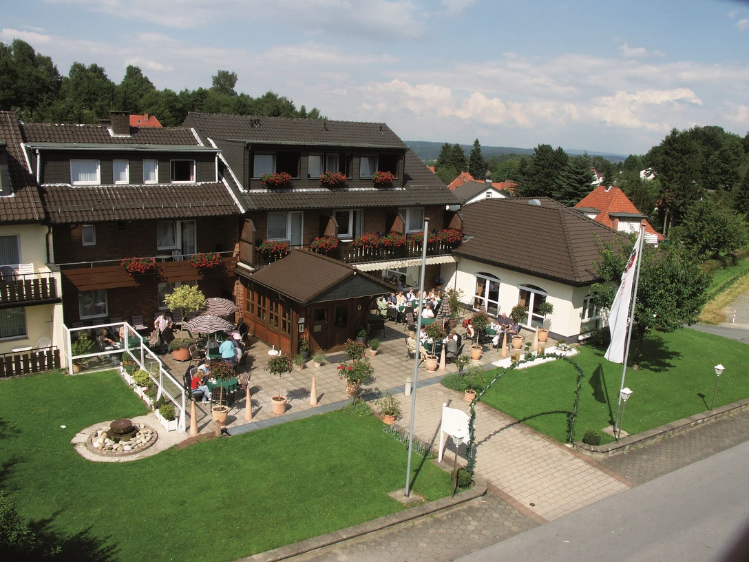 Zweistöckiges Gästehaus mit Blumenbalkonen und Terrasse, umgeben von gepflegtem Garten, Voralpen.