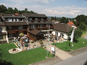 aussenansicht_haus-weber Zweistöckiges Gästehaus mit Blumenbalkonen und Terrasse, umgeben von gepflegtem Garten, Voralpen.