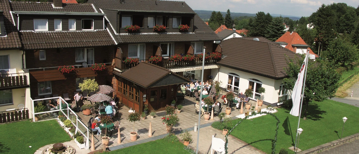 aussenansicht_haus-weber Zweistöckiges Gästehaus mit Blumenbalkonen und Terrasse, umgeben von gepflegtem Garten, Voralpen.