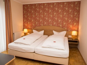 hilckmann-125 Zwei nebeneinander stehende Einzelbetten in einem Hotelzimmer mit gemustertem roten Wandteppich.