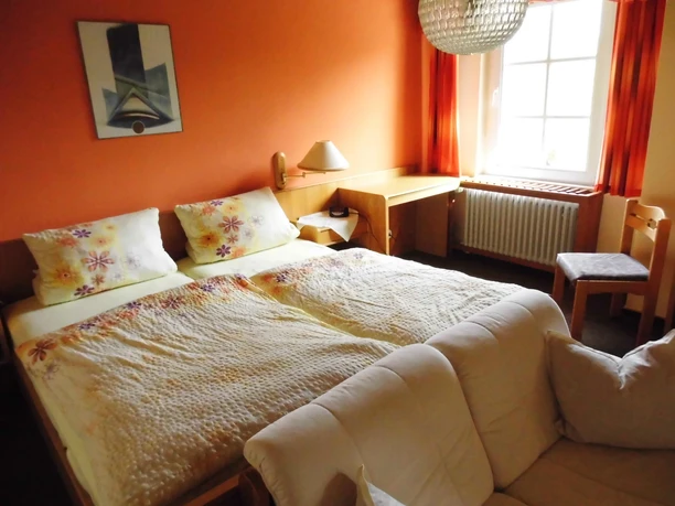 Ein lichtdurchflutetes Doppelzimmer mit zwei Betten, Schreibtisch und gemütlichem Sofa.