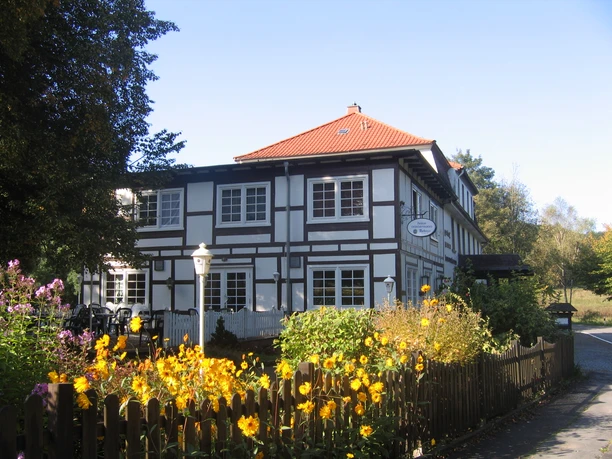 Historisches Fachwerkhaus mit roten Dachziegeln, umgeben von blühendem Garten und Holzzaun im Sommer.
