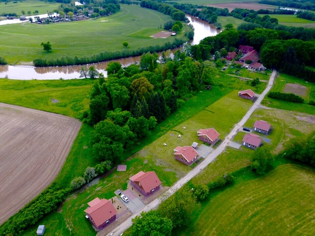 fereinh-user-emsland-luftbild-1 Luftaufnahme mehrerer Ferienhäuser mit roten Dächern nahe Fluss, umgeben von Feldern und Wiesen