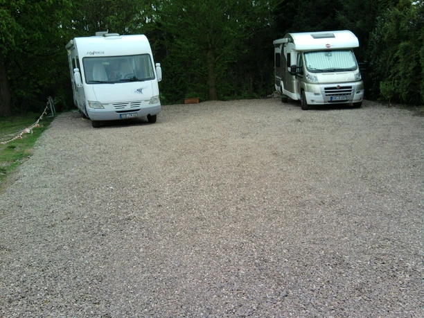 Eifgen-Sauna Zwei Wohnmobile stehen auf einem unbefestigten Kiesplatz, umgeben von grünen Bäumen.