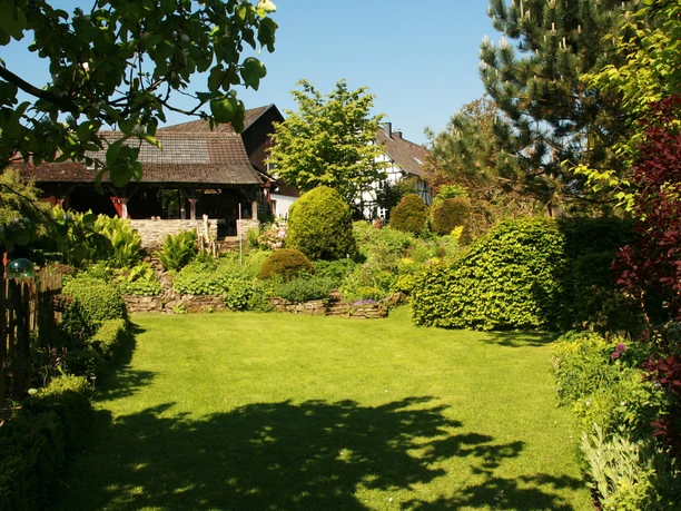 Garten Ein gepflegter Garten mit grünem Rasen, umgeben von Hecken und Bäumen, vor einem Landhaus.