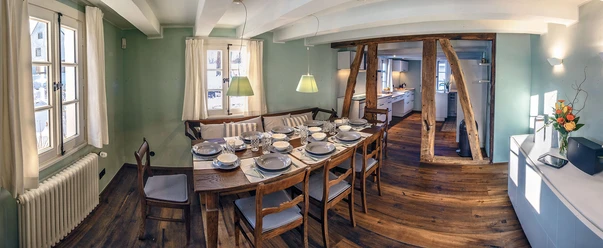 Ferienhaus "Hassel 14" Ein gemütliches Esszimmer mit Holzfußboden, gedecktem Tisch und rustikalen Holzbalken an der Wand.