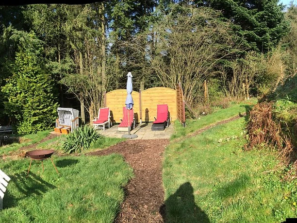Ferienhaus Ketzberg Sonnige Terrasse mit Liegestühlen, Sonnenschirmen und einem Garten mit umliegenden Bäumen.