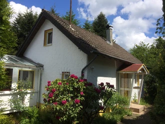 Ferienhaus Ketzberg Ein weißes Einfamilienhaus mit Satteldach, umgeben von blühenden Rhododendron und grünen Bäumen.