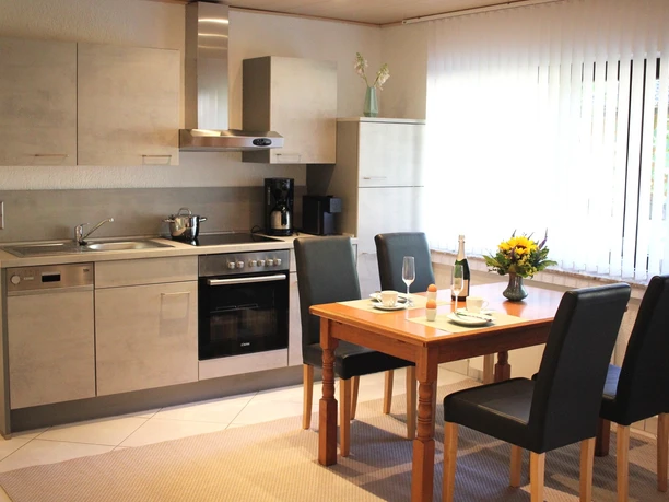 Küche Moderne Küche mit Edelstahlgeräten, Essbereich mit Holztisch und vier schwarzen Stühlen, hell beleuchtet.