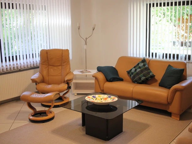 Wohnzimmer Modernes Wohnzimmer mit Ledercouch, passendem Sessel, Couchtisch aus Glas und großen Fenstern.