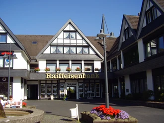 Außenansicht Fachwerkhaus im typisch deutschen Stil, Eingang zur Raiffeisenbank mit Blumenbeet im Vordergrund.