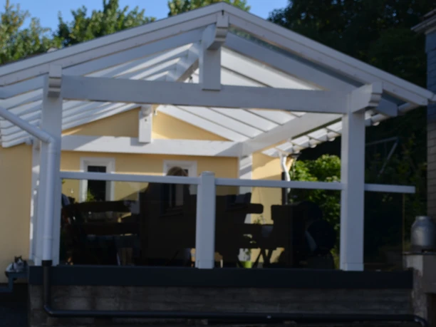 Ferienwohnung Bergisch Land Gemütliche Terrasse mit weißem Holzpavillon, unter einem sonnenüberfluteten transparenten Dach.