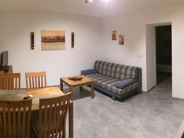 Ferienwohnung Blissenbach Wohnzimmer mit Esstisch, vier Stühlen, Sofa, Couchtisch und dekorativen Bildern an weißen Wänden.