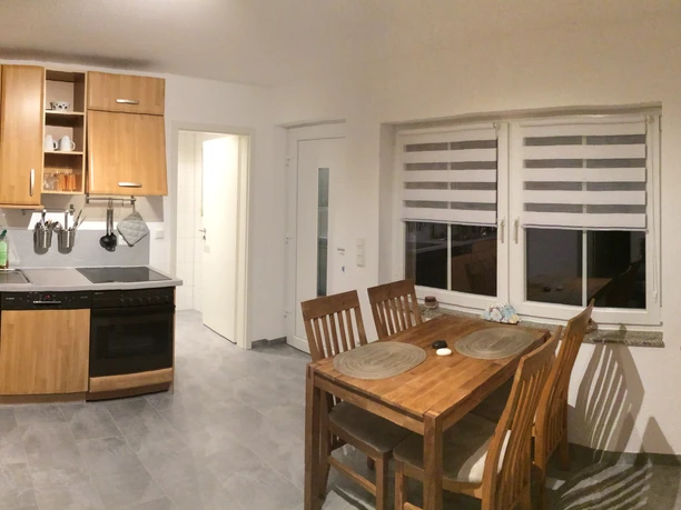 Ferienwohnung Blissenbach Kompakte Küchenzeile mit Herd und Mikrowelle, daneben Esstisch mit vier Stühlen in gemütlichem Raum.