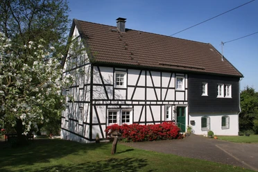 Ferienhaus Casa Maria Fachwerkhaus mit roten Blumen im Vordergrund, umgeben von grüner Wiese und Bäumen.