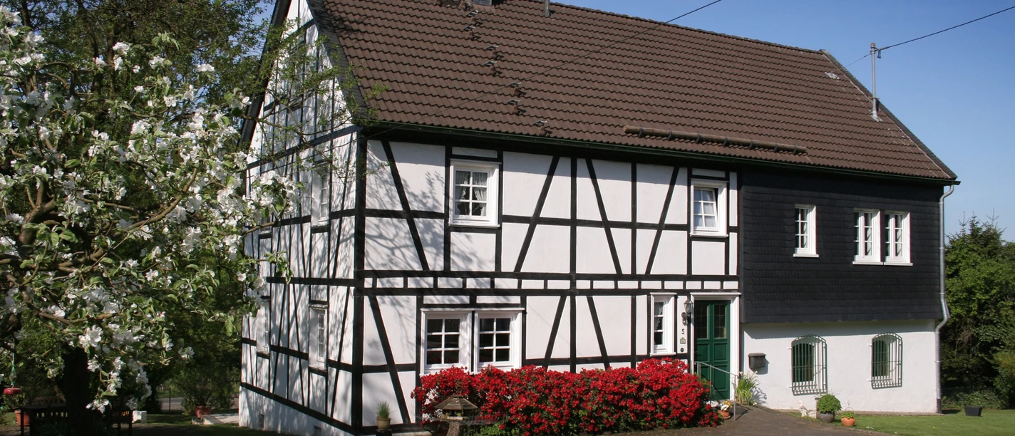 Ferienhaus Casa Maria Fachwerkhaus mit roten Blumen im Vordergrund, umgeben von grüner Wiese und Bäumen.