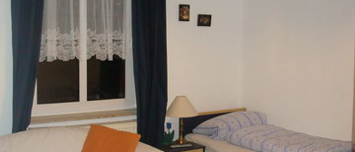 Schlafzimmer Kleine, gemütliche Wohnraumecke mit Einzelbett, Sofa, Tisch und großem Fenster mit dunklen Vorhängen.