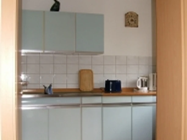 Küche Kompakte Küche mit hellblauen Schränken, gefliester Rückwand, Holzarbeitsplatten und Terrakottaboden.