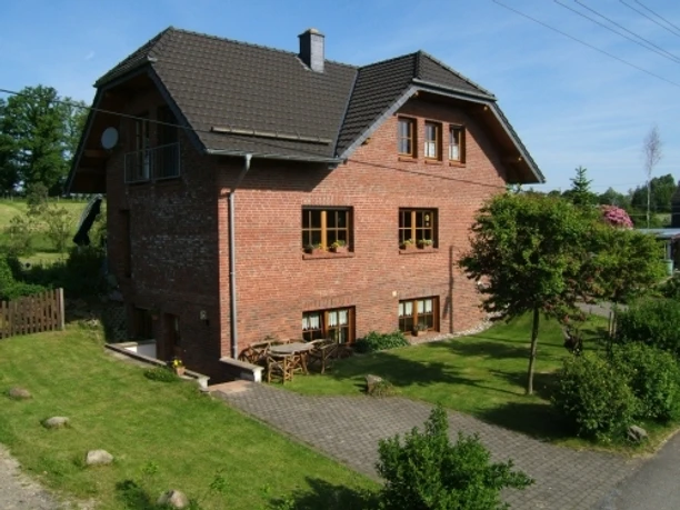 Ferienwohnung Happ Backsteinhaus mit Satteldach, umgeben von gepflegtem Garten und gepflastertem Weg, ländliche Umgebung.