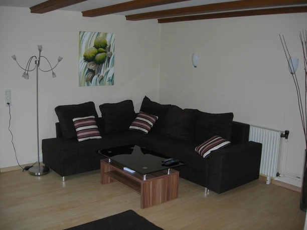 Wohnzimmer Gemütliches Wohnzimmer mit braunem Ecksofa, Glastisch, Stehlampe und Wandbild mit grünen Akzenten.