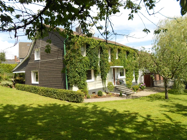 Außenansicht Ein charmantes, mit Efeu bewachsenes Wohnhaus inmitten eines grünen Gartens und strahlender Sonne.