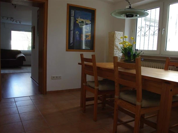 Esszimmer Essbereich mit Holzmöbeln, dekoriert mit einem Blumenstrauß, angrenzend an ein helles Wohnzimmer.