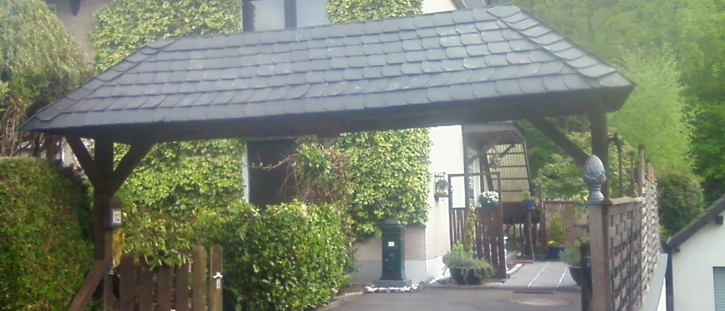 Außenansicht Haus mit Dachbegrünung und ein überdachter Carport in einer ruhigen, grünen Wohngegend.