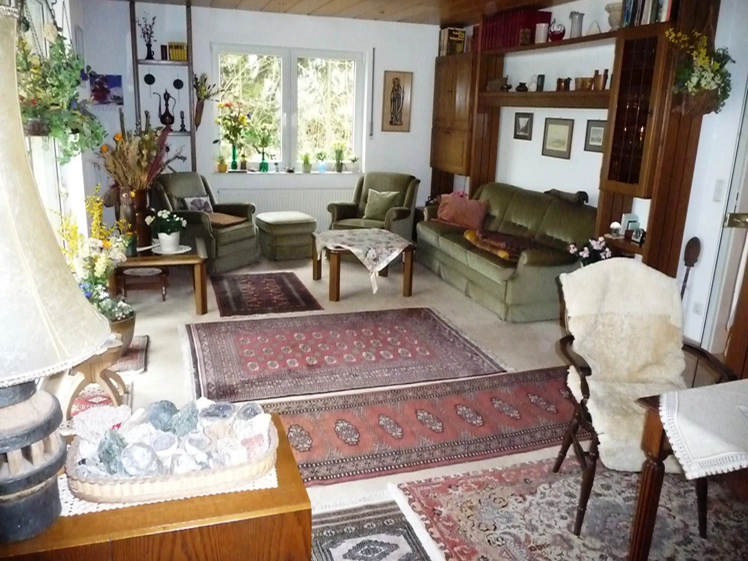 Ferienwohnung Kutnar Gemütliches Wohnzimmer mit grüner Sofagarnitur, Perserteppichen, Pflanzen und großen Fenstern.