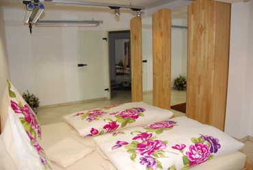 Schlafzimmer Schlafzimmer mit Doppelbett, Holzwänden und floralem Bettzeug, im Hintergrund ein offener Durchgang.