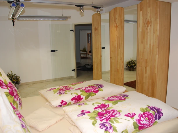 Schlafzimmer Schlafzimmer mit Doppelbett, Holzwänden und floralem Bettzeug, im Hintergrund ein offener Durchgang.