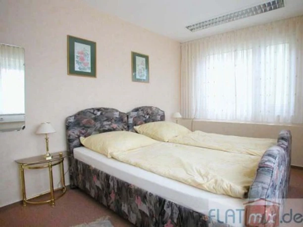 Schlafzimmer Doppelbettzimmer mit hellen Wänden, zwei Nachttischen und einem Fenster mit weißen Vorhängen.