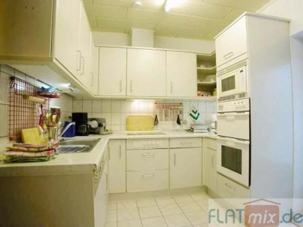 Küche Helle Küche mit weißen Schränken, Einbauherd, Mikrowelle und Fliesenboden in einem modernen Stil.