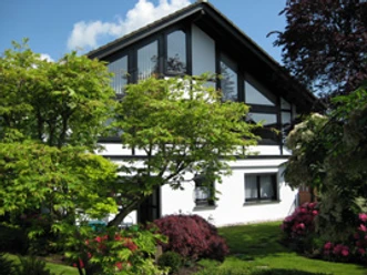 Aussenansicht Modernes zweistöckiges Haus mit schwarz-weißer Fassade, umgeben von gepflegtem, blühendem Garten.