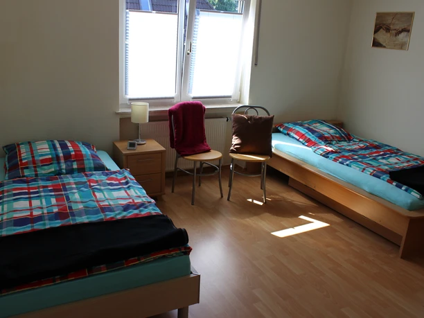 Schlafzimmer Zwei helle Einzelbetten mit bunter Bettwäsche in einem lichtdurchfluteten Raum mit Fenster.