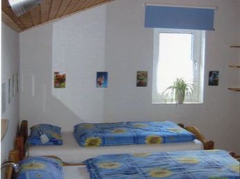 Ferienwohnung Haas Gemütliches Gästezimmer mit zwei Einzelbetten, blauer Bettwäsche, Holzdecke und kleinem Fenster.
